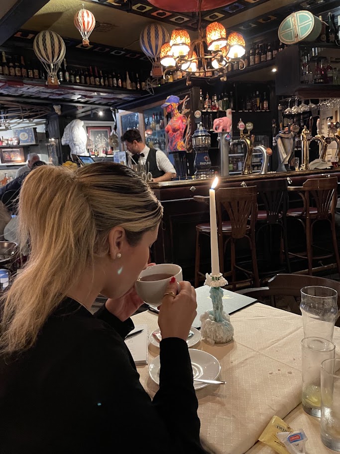 Tata tomando uma bebida em uma xícara, à mesa com uma vela acesa